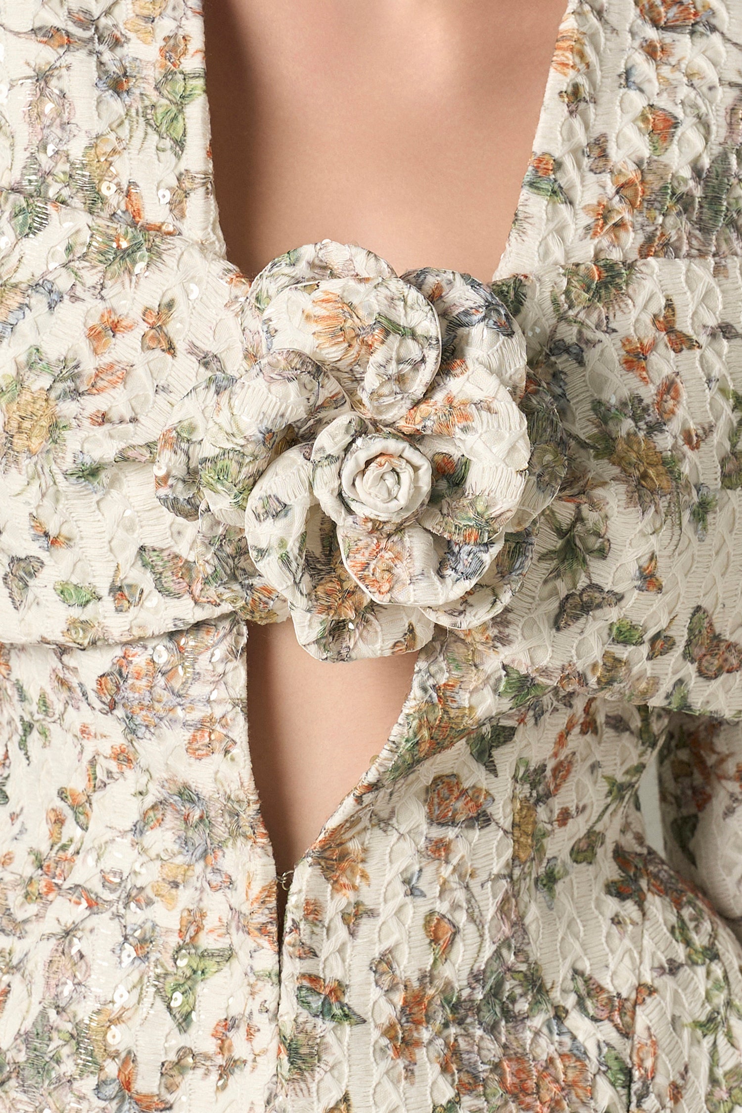 The jacket features a deep V neckline adorned with a handcrafted floral accent.