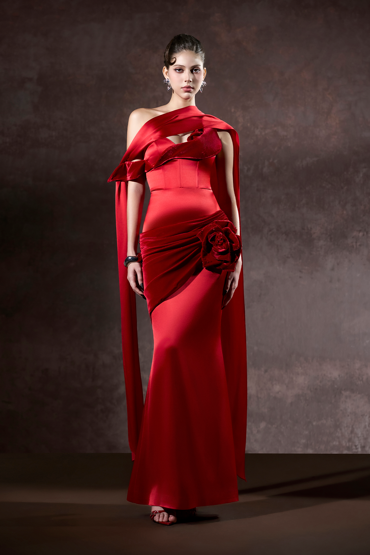 Woman wearing a red one-shoulder evening gown against a dark background
