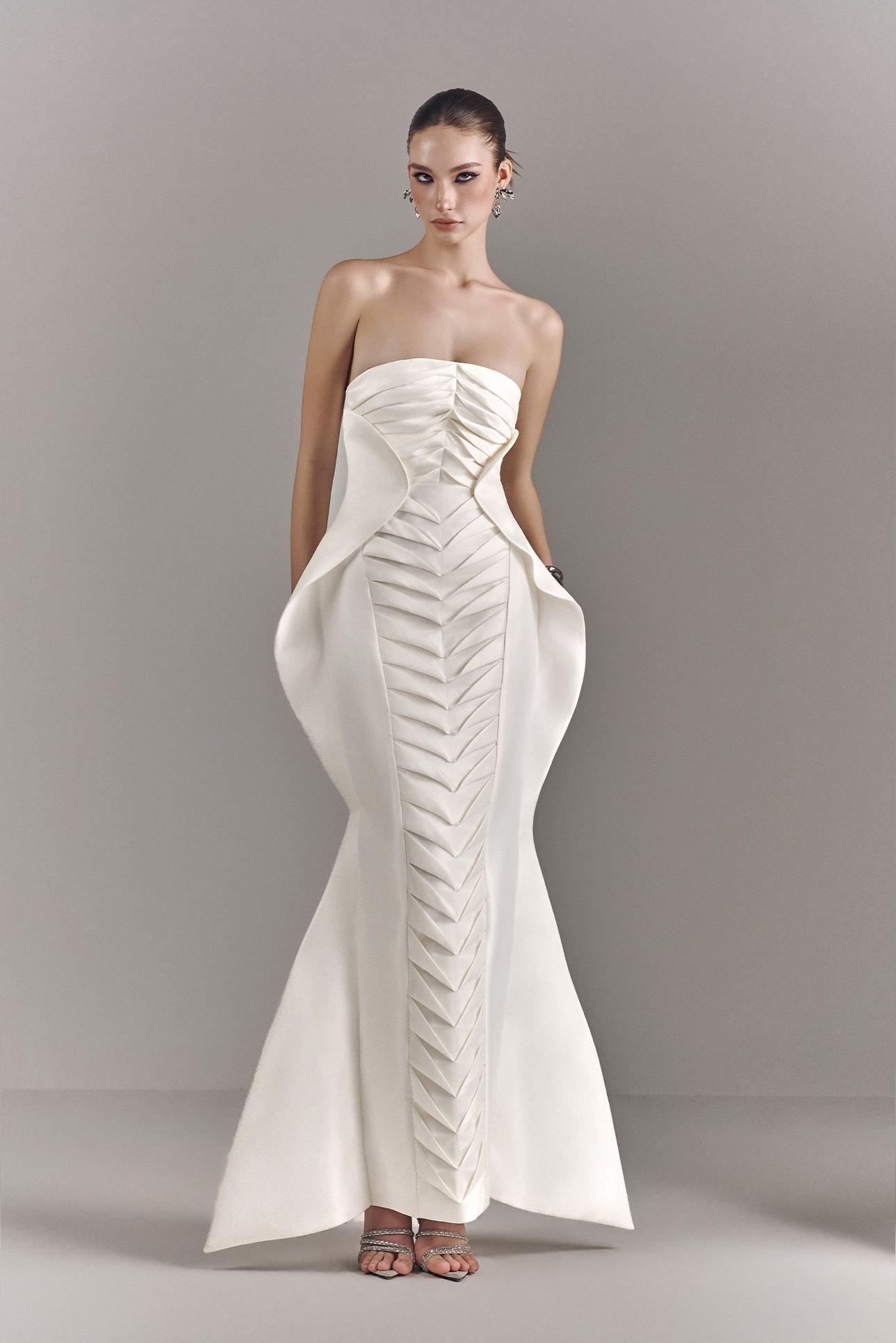 Woman wearing a strapless white evening gown against a plain background
