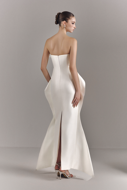 Woman wearing a strapless white evening gown with a slit on a plain background