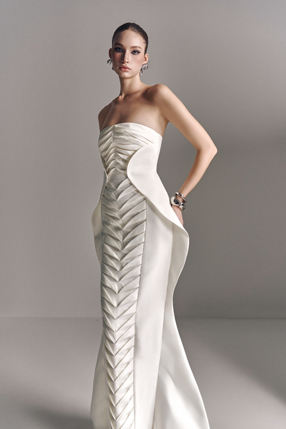 Woman wearing a strapless white evening gown with feather-like design on a plain background