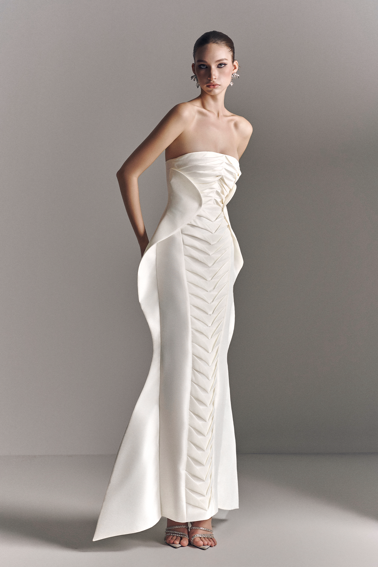 Woman wearing a strapless white evening gown with a high slit on a plain background