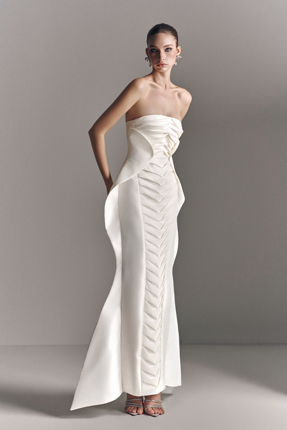 Woman wearing a strapless white evening gown with a high slit on a plain background