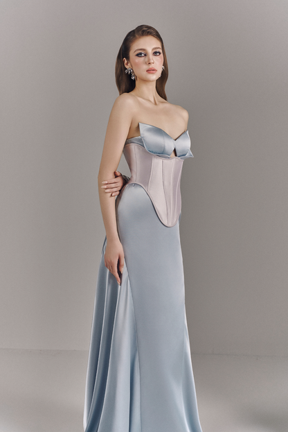 Woman wearing a strapless evening gown with a fitted bodice and flowing skirt on a plain background