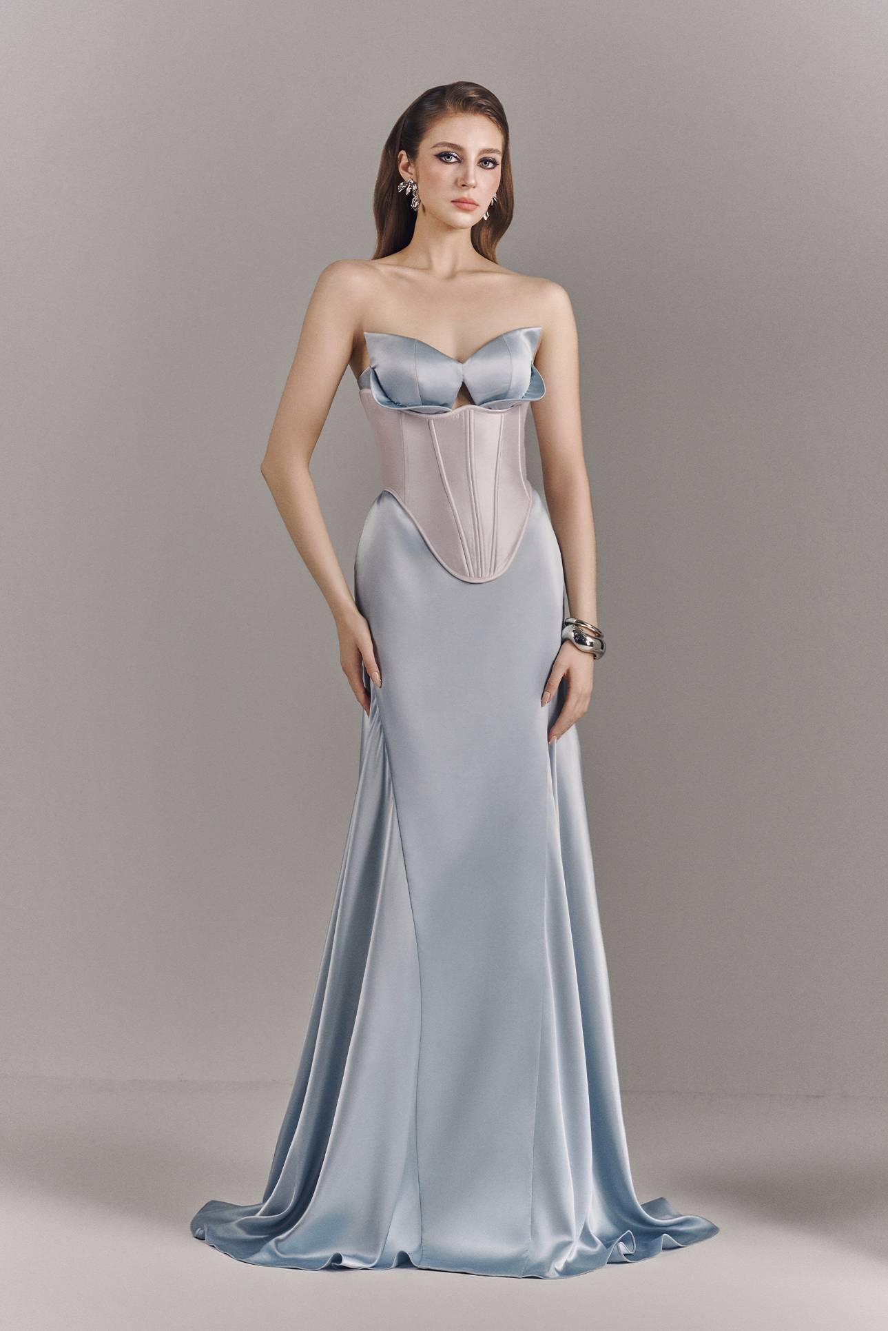 Woman wearing a strapless evening gown with a fitted bodice and flowing skirt on a plain background