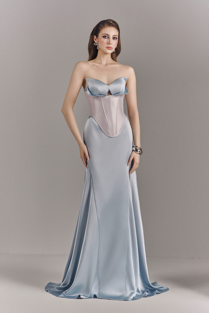 Woman wearing a strapless evening gown with a fitted bodice and flowing skirt on a plain background