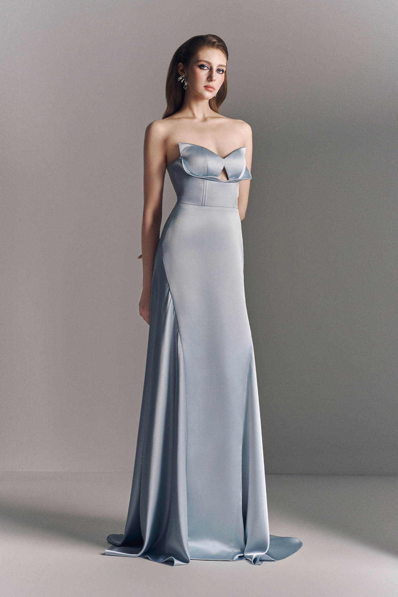 Woman wearing a strapless, floor-length light blue gown against a neutral background