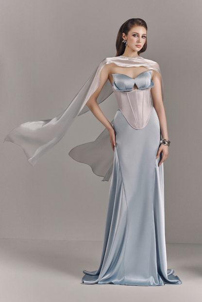 Woman wearing a light blue evening gown with a flowing train on a gray background