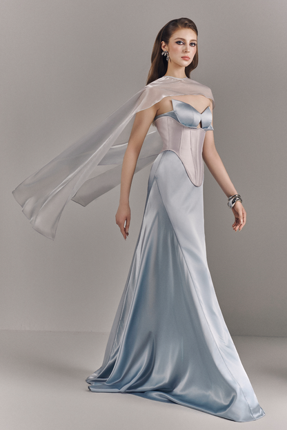 Woman wearing a light blue evening gown with a sheer overlay against a gray background