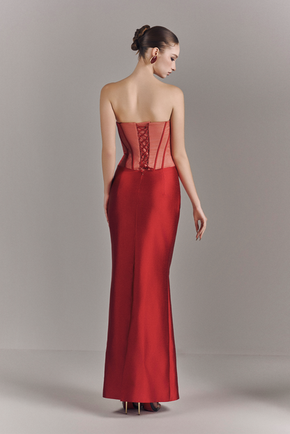 Woman wearing a red strapless evening gown with a lace-up back on a plain background