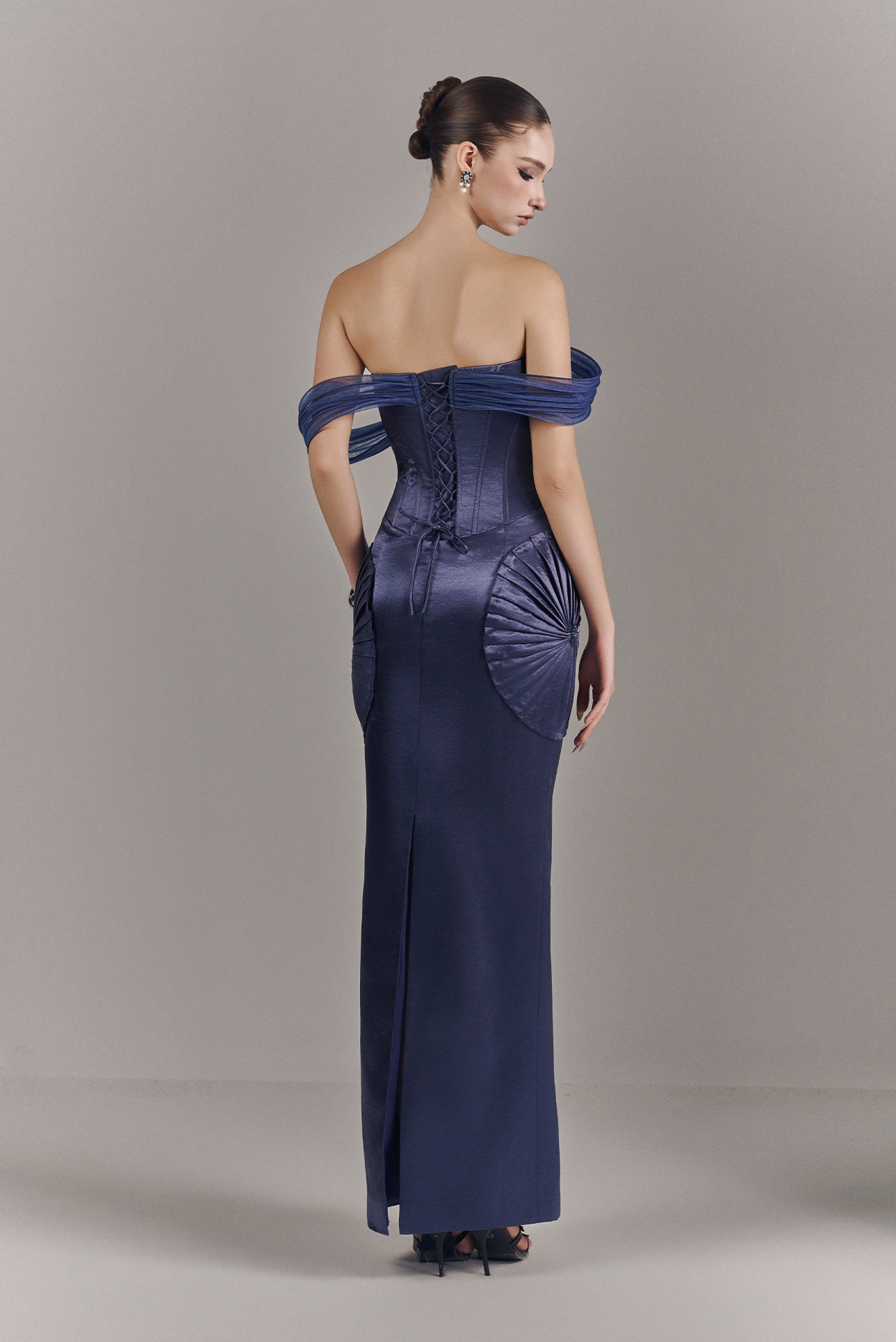Woman wearing a long, off-shoulder blue dress against a plain background