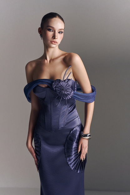 Woman wearing a blue off-shoulder dress with floral details against a gray background