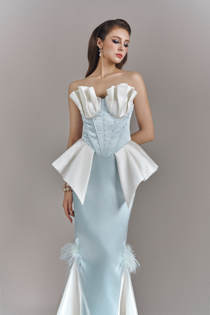 Woman wearing a light blue and white evening gown with feather details on a gray background