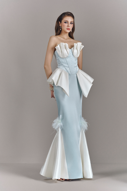 Woman wearing a strapless evening gown with ruffled top and feather details on a plain background