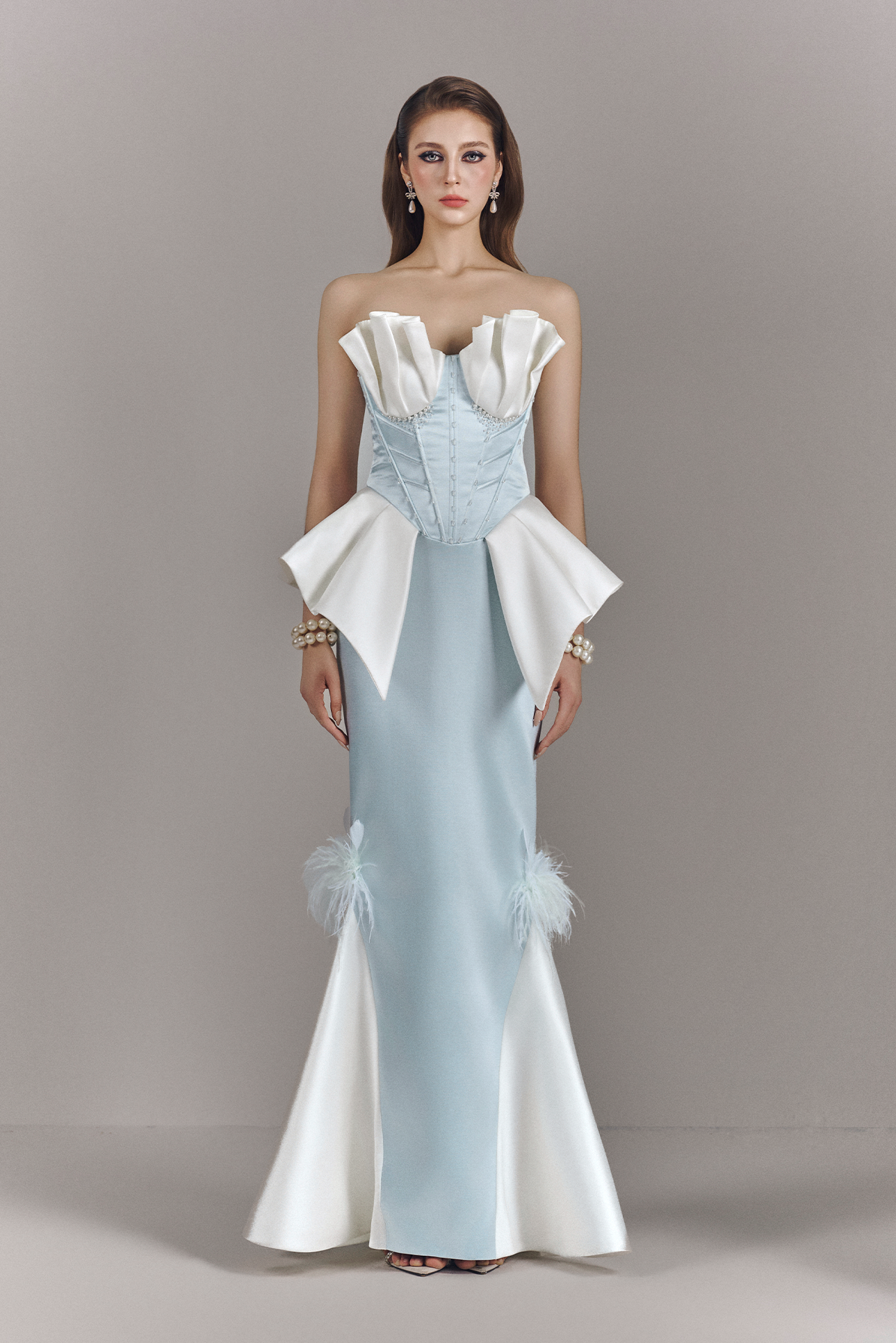 Woman wearing a light blue and white evening gown with ruffled details on a gray background