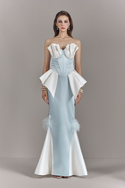 Woman wearing a light blue and white evening gown with ruffled details on a gray background