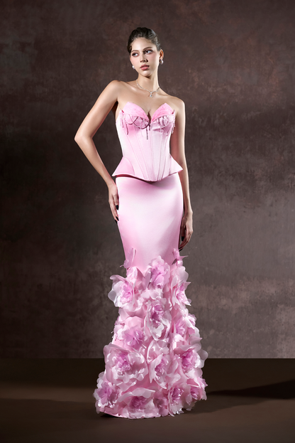 Woman wearing a pink evening gown with floral details against a dark background