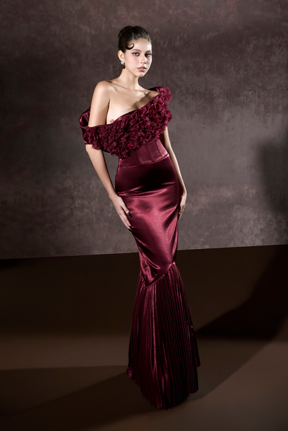 Woman wearing a burgundy evening gown with floral details against a dark background