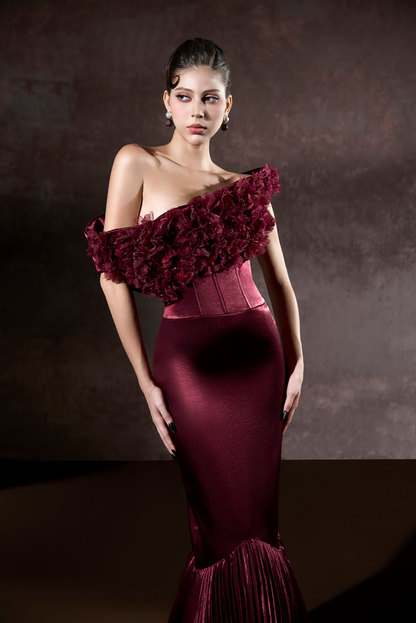 Woman wearing a burgundy evening gown with floral details against a dark background