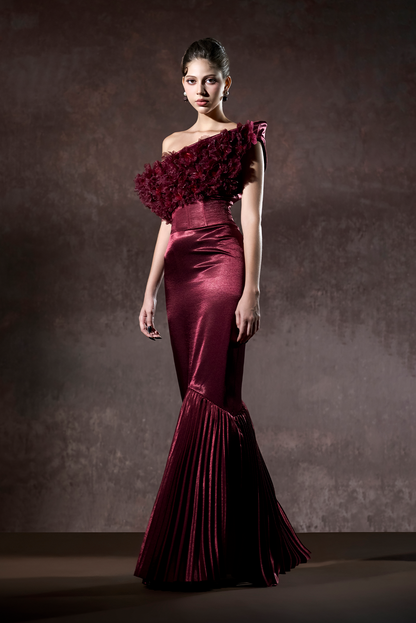 Woman wearing a burgundy one-shoulder gown with floral details against a dark background
