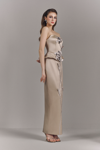 Woman wearing a beige strapless gown with floral details on a plain background