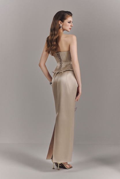 Woman wearing a beige strapless gown with a slit on a plain background