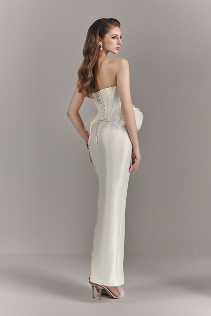 Woman wearing a strapless white evening gown against a gray background
