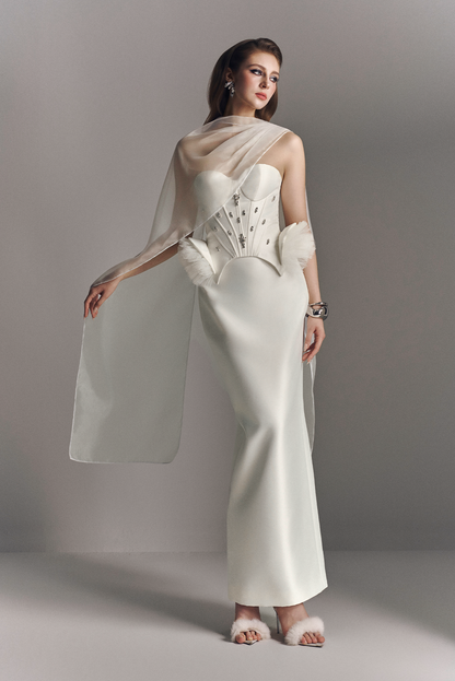 Woman wearing a white bridal gown with a shawl against a gray background