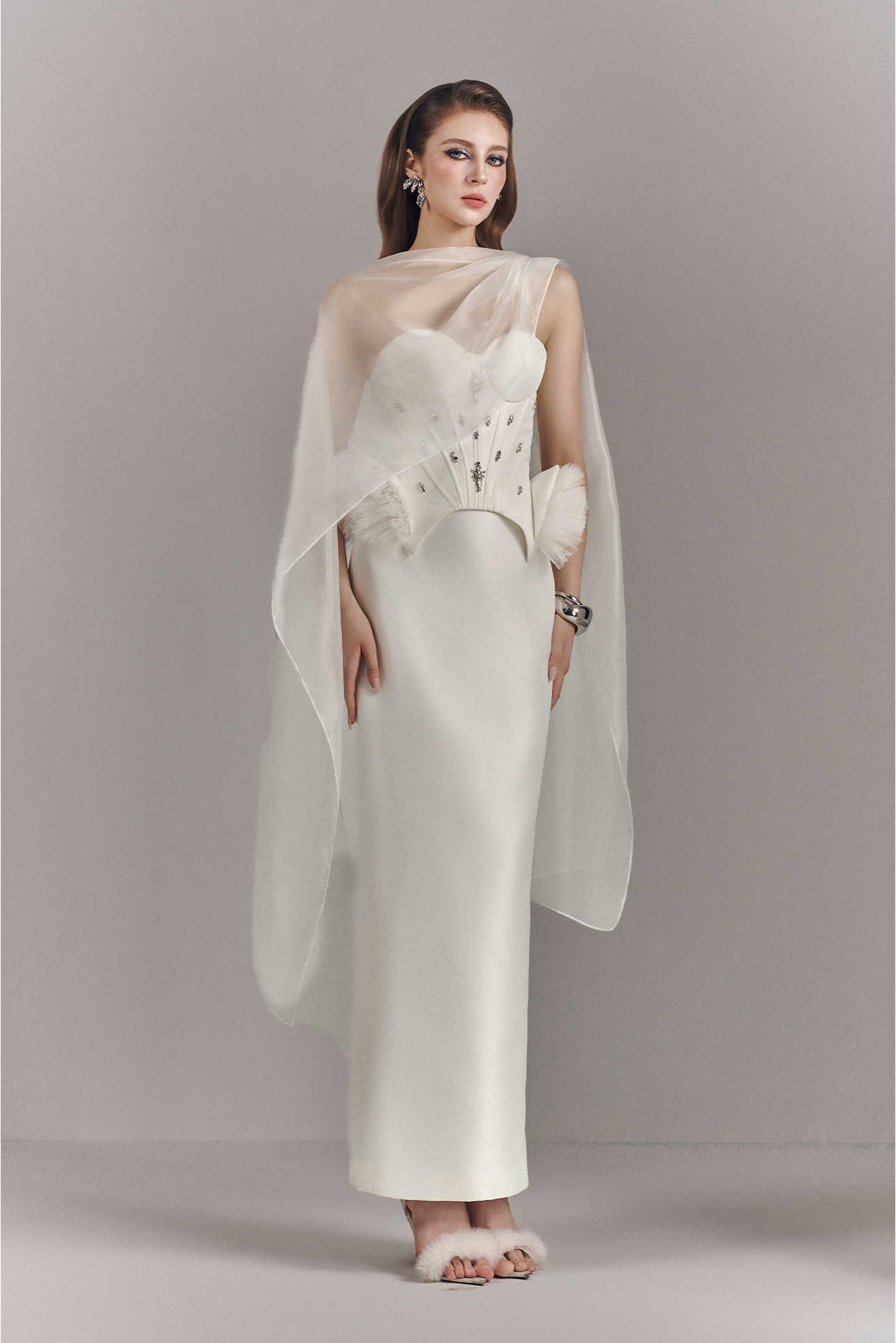 Woman wearing a white dress with a sheer overlay against a plain background
