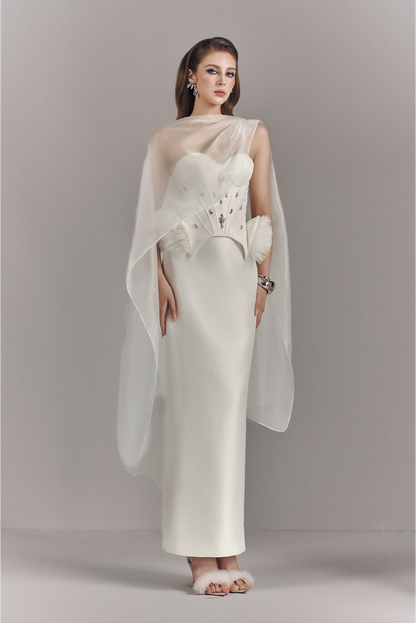 Woman wearing a white dress with a sheer overlay against a plain background