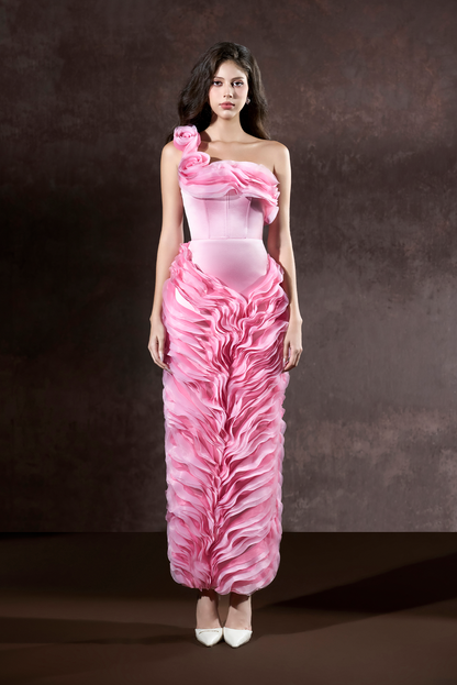 Woman wearing a pink strapless gown with ruffled details against a brown background
