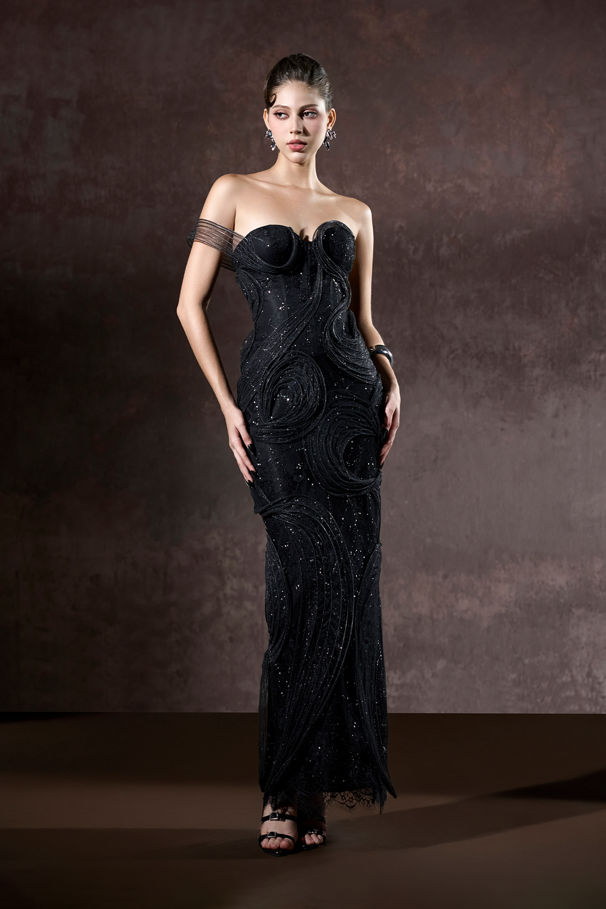Woman wearing a black strapless gown with intricate detailing against a brown background