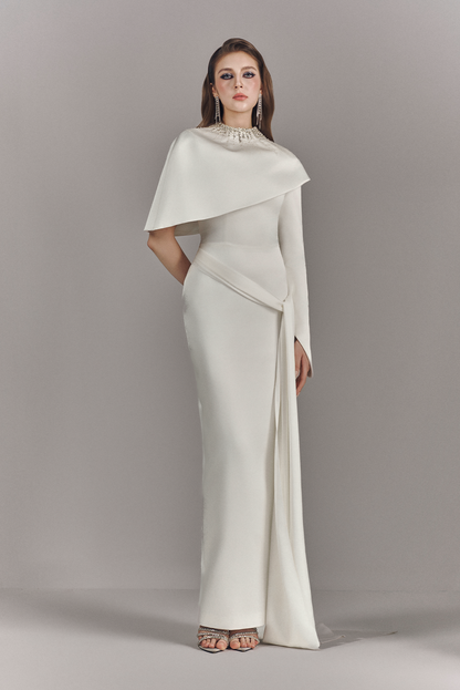 Woman wearing a white evening gown with a cape against a gray background