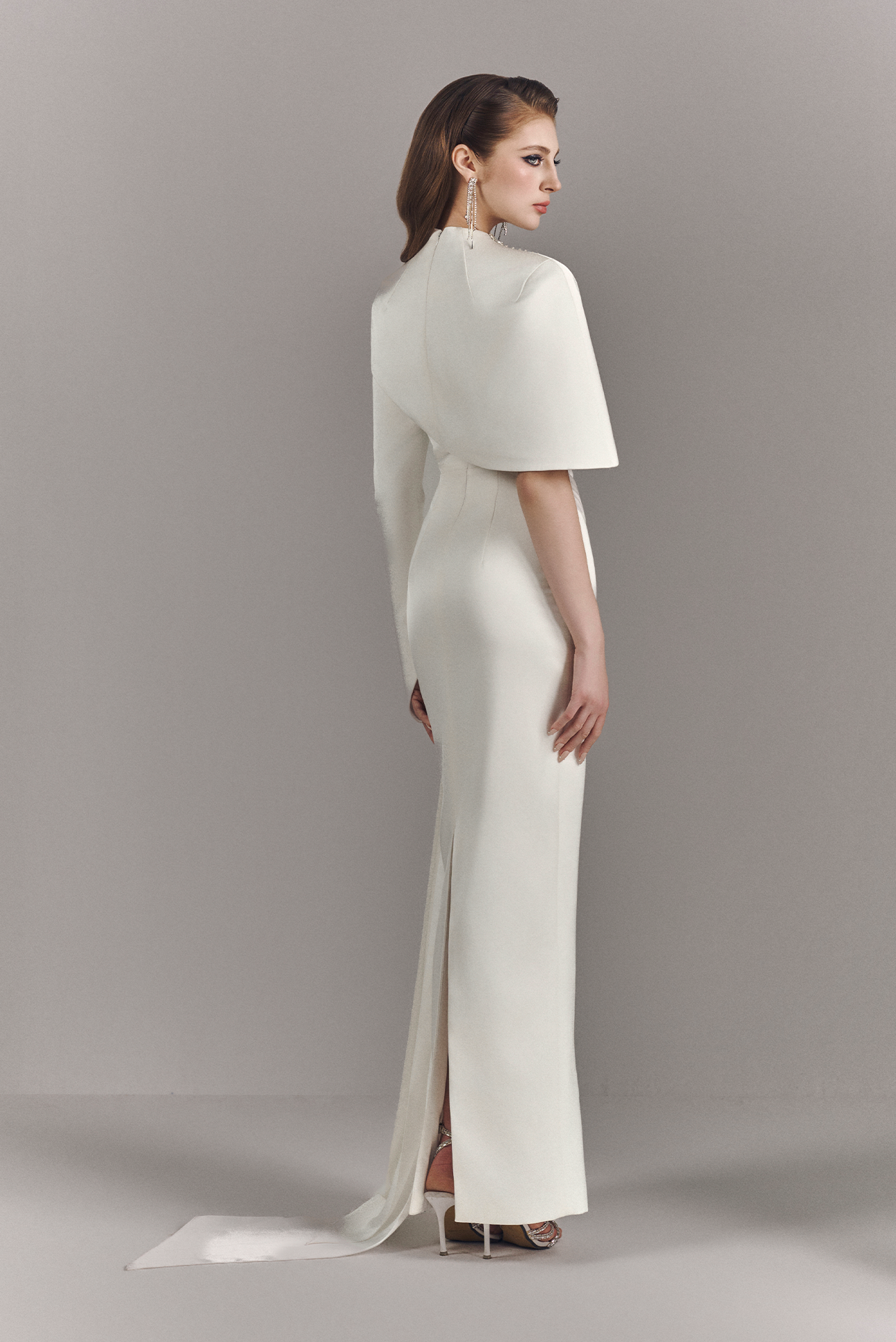 Woman wearing a white evening gown with a cape on a gray background