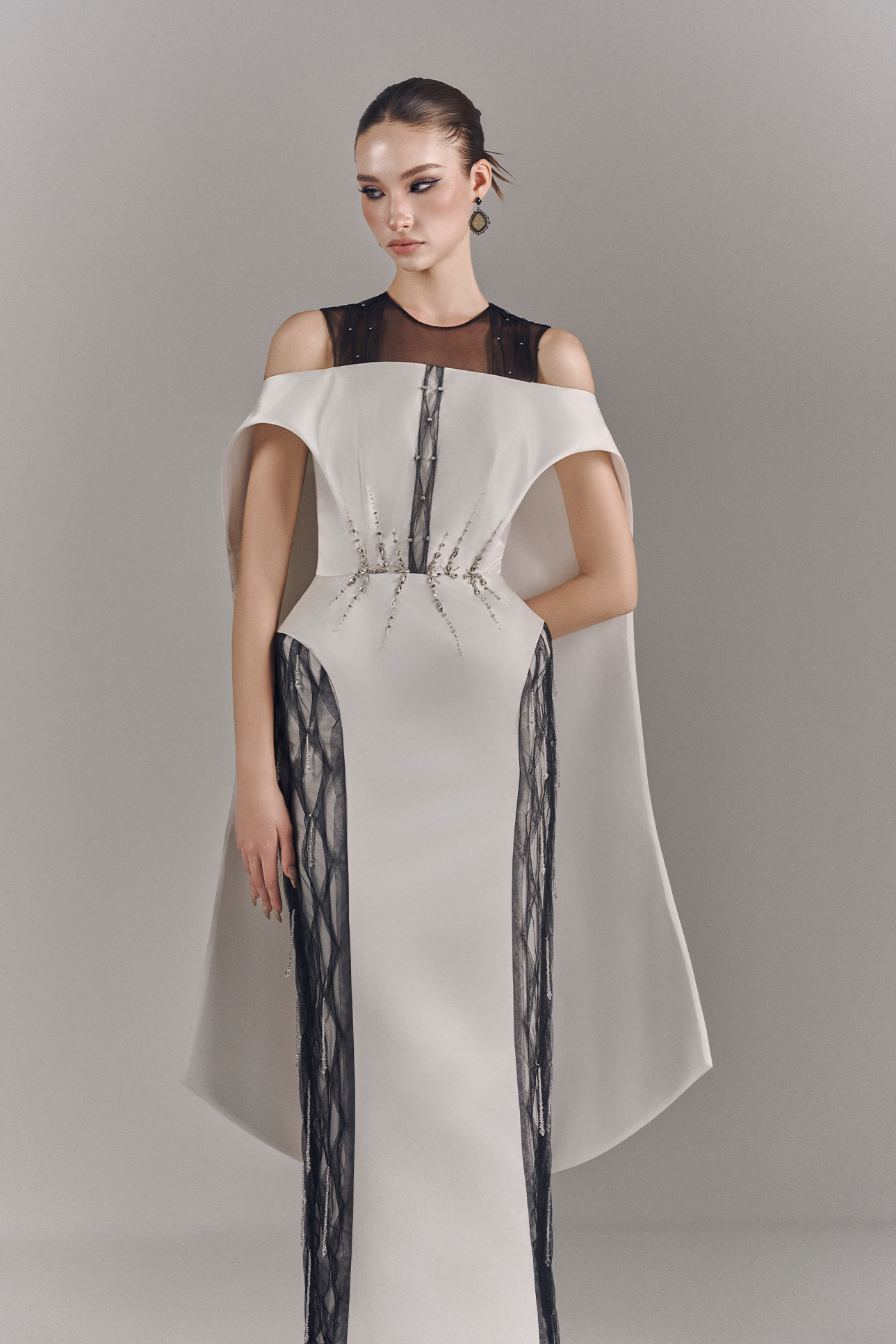 Model wearing a white off-shoulder dress with black mesh panels on a gray background