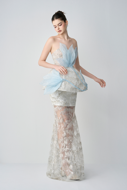 Woman wearing a light blue and silver dress with floral patterns on a white background