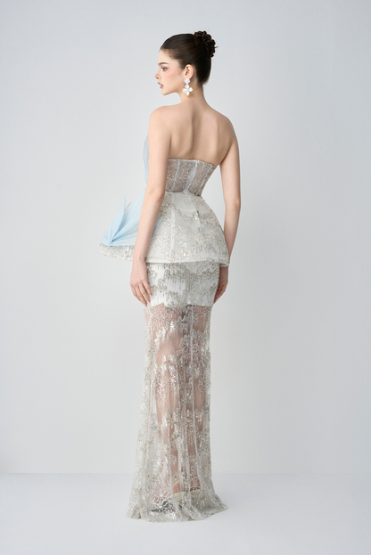 Woman wearing a strapless, patterned evening gown on a plain background