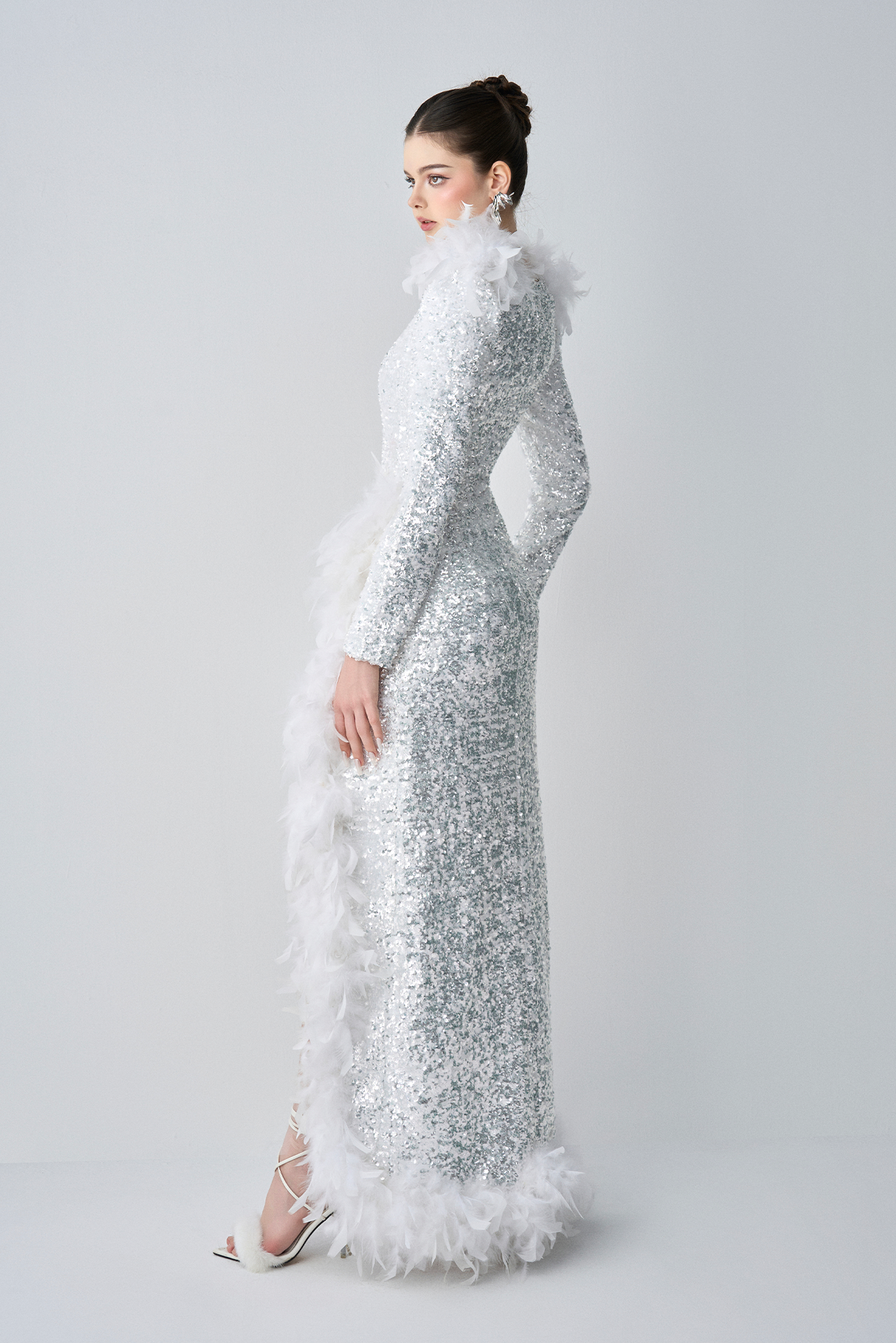 Woman wearing a silver sequin gown with feather details on a white background