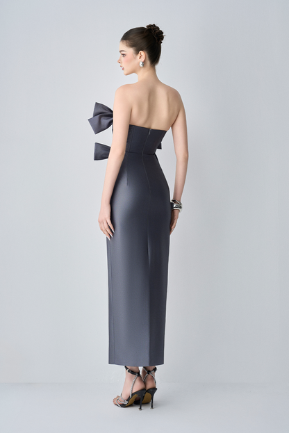 Woman wearing a strapless evening gown with a large bow detail on a white background
