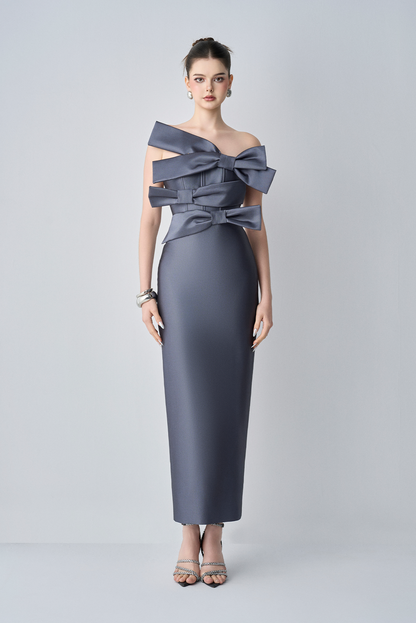 Woman wearing a gray dress with a large bow detail on a light gray background