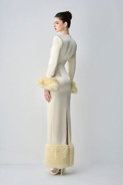 Woman wearing a long, elegant dress with fur trim on a plain background