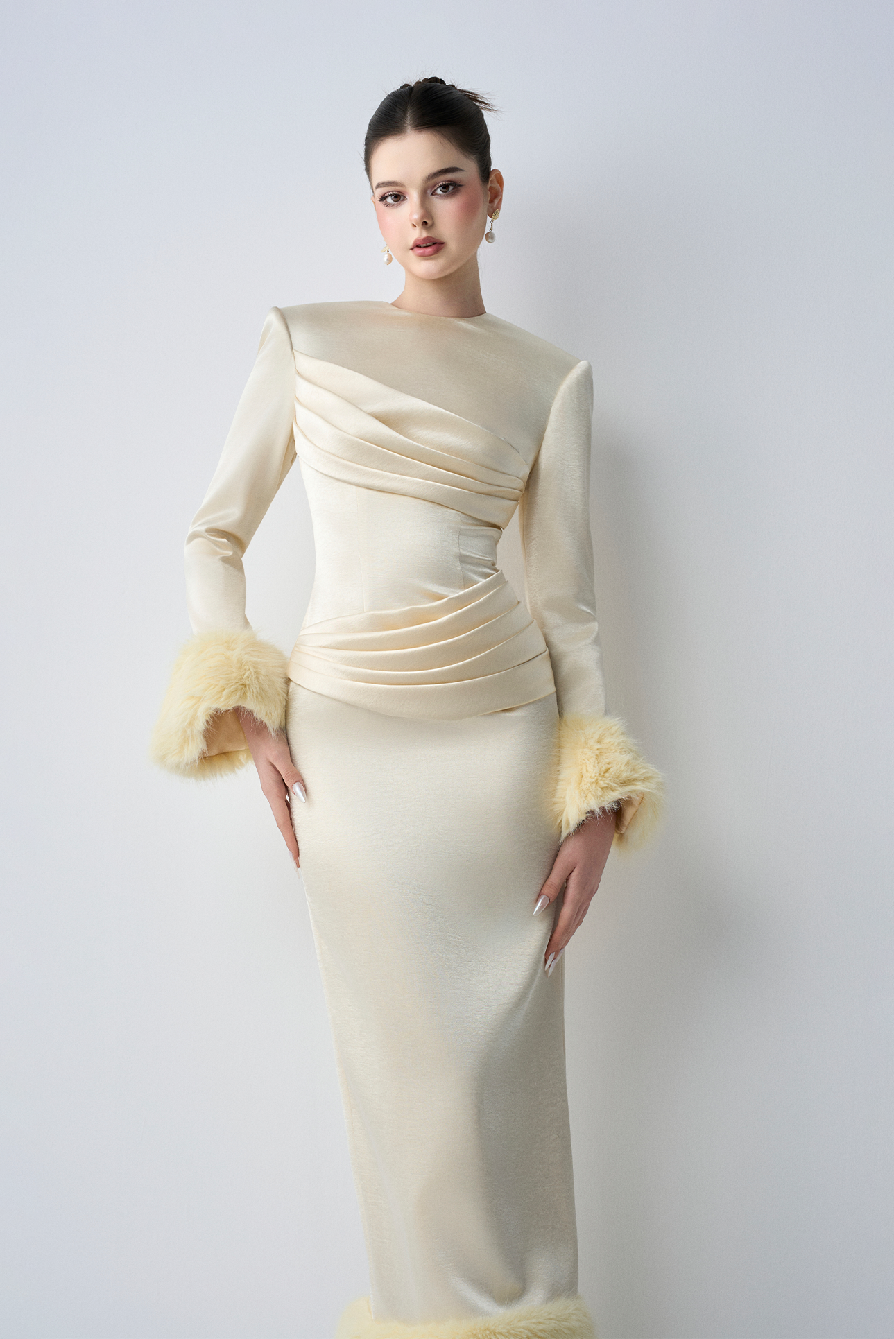 Woman wearing a cream-colored evening gown with fur cuffs on a white background