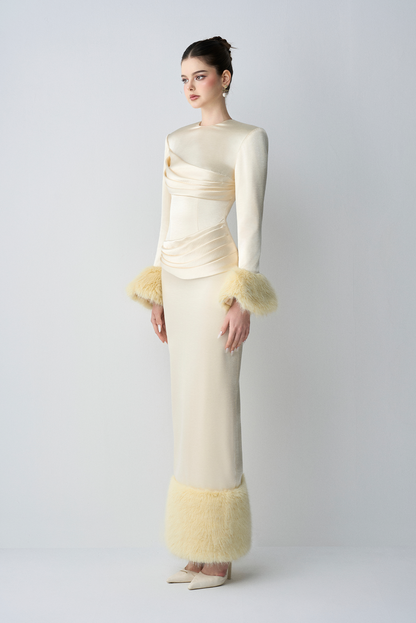 Woman wearing a cream-colored evening gown with feathered cuffs on a white background
