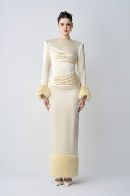 Woman wearing a long, cream-colored dress with ruffled sleeves on a white background