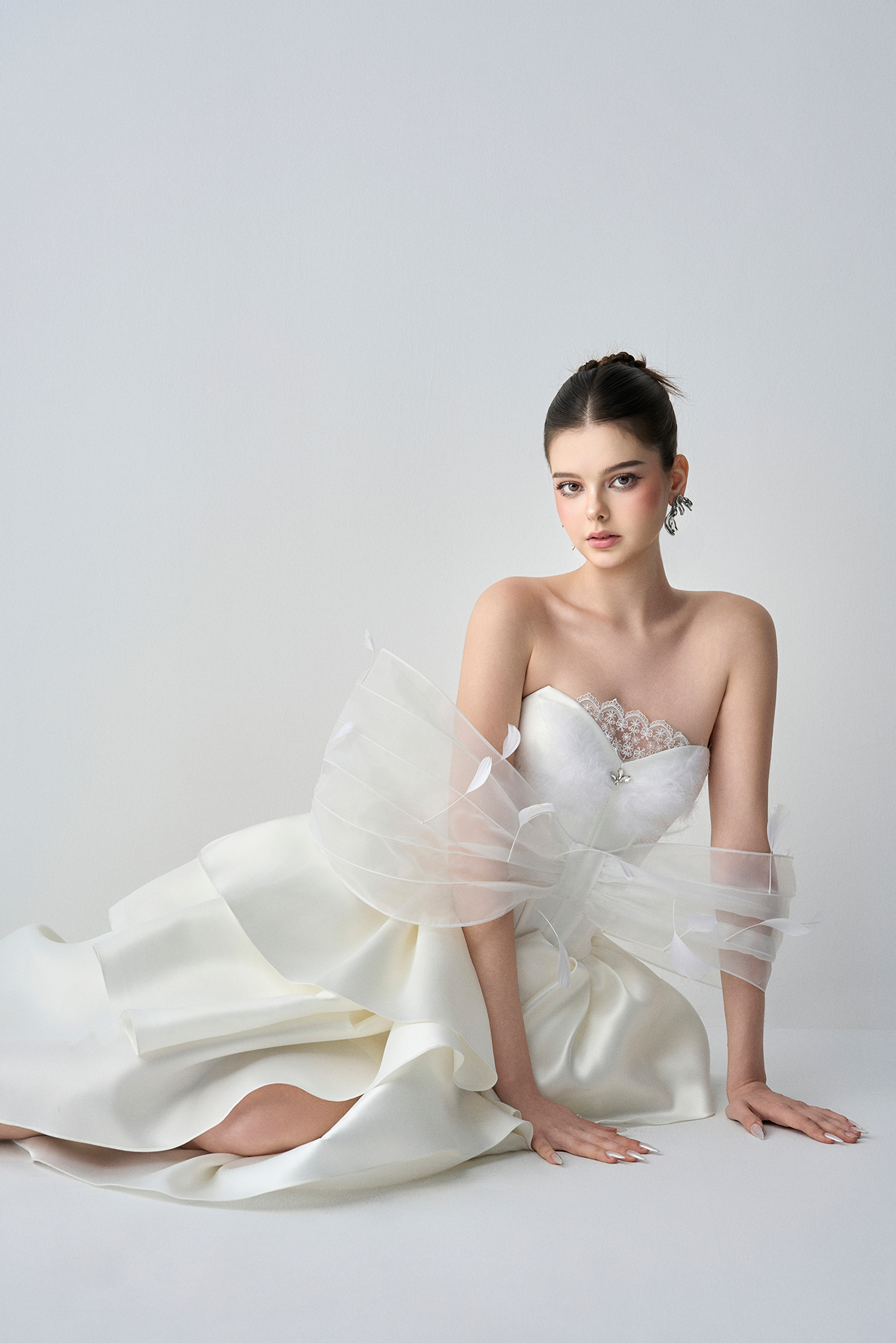 Woman in a white strapless gown with a sheer overlay on a light gray background