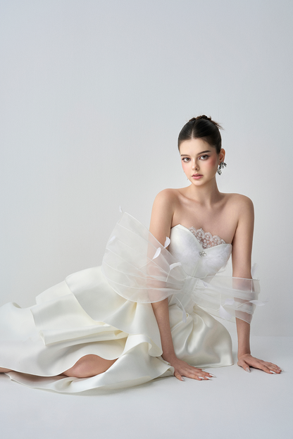 Woman in a white strapless gown with a sheer overlay on a light gray background