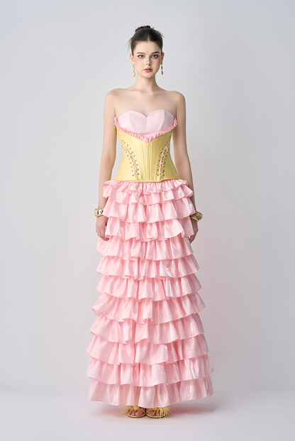 Woman wearing a pink and yellow strapless gown with ruffled layers on a white background