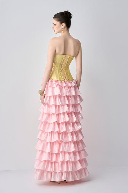 Woman wearing a strapless yellow top and pink ruffled gown on a white background
