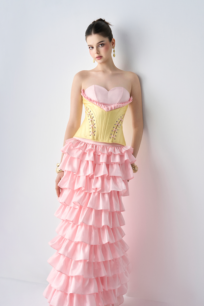 Woman wearing a yellow top and pink ruffled skirt against a white background