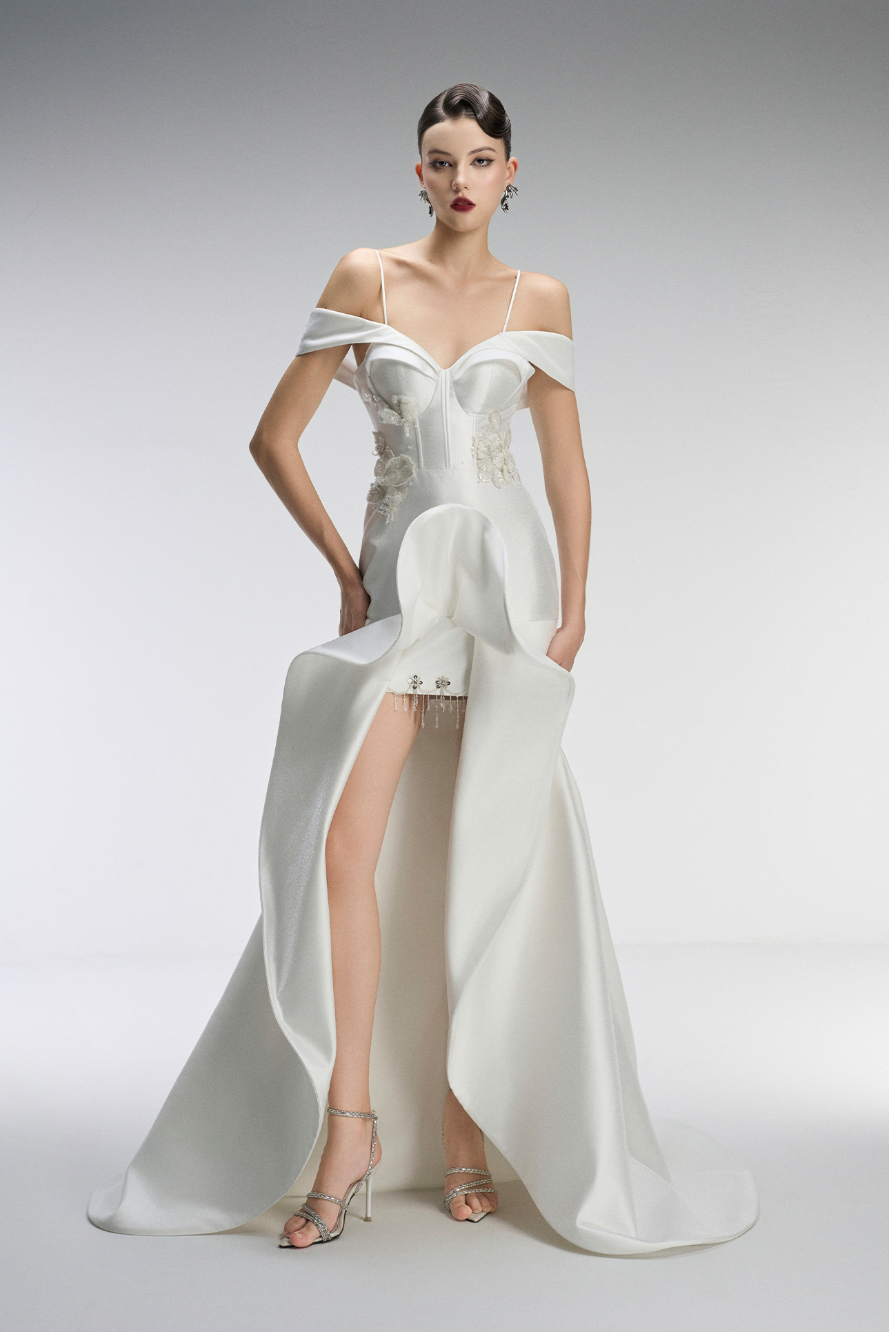 Model wearing a white off-shoulder evening gown with a high slit on a gray background